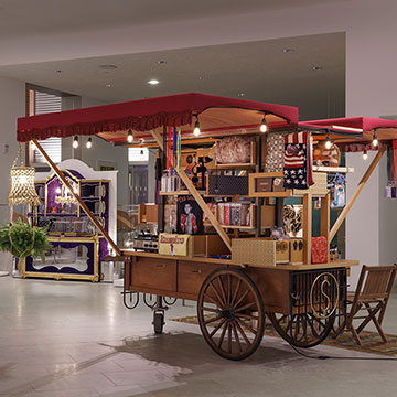 A view of an art installation at the Nerman Museum by Carlos Rolon showcasing a large rolling cart with sides that have been extended revealing various items housed within it