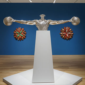 A silver sculpture depicting the torso and arms of a basketball player. His arms are outstretched and he's palming a basketball in each hand.
