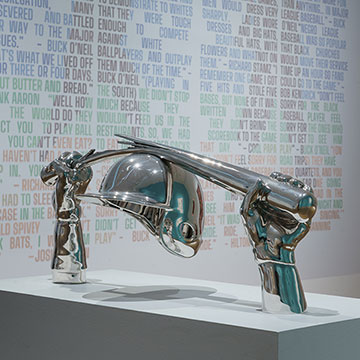 A silver sculpture of a bat being broken over a helmet